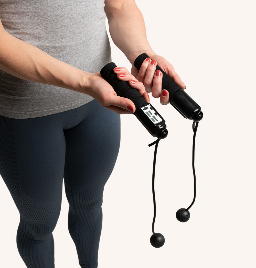 Frau hält Springseile. Sie trägt Leggings und hält die Griffe.