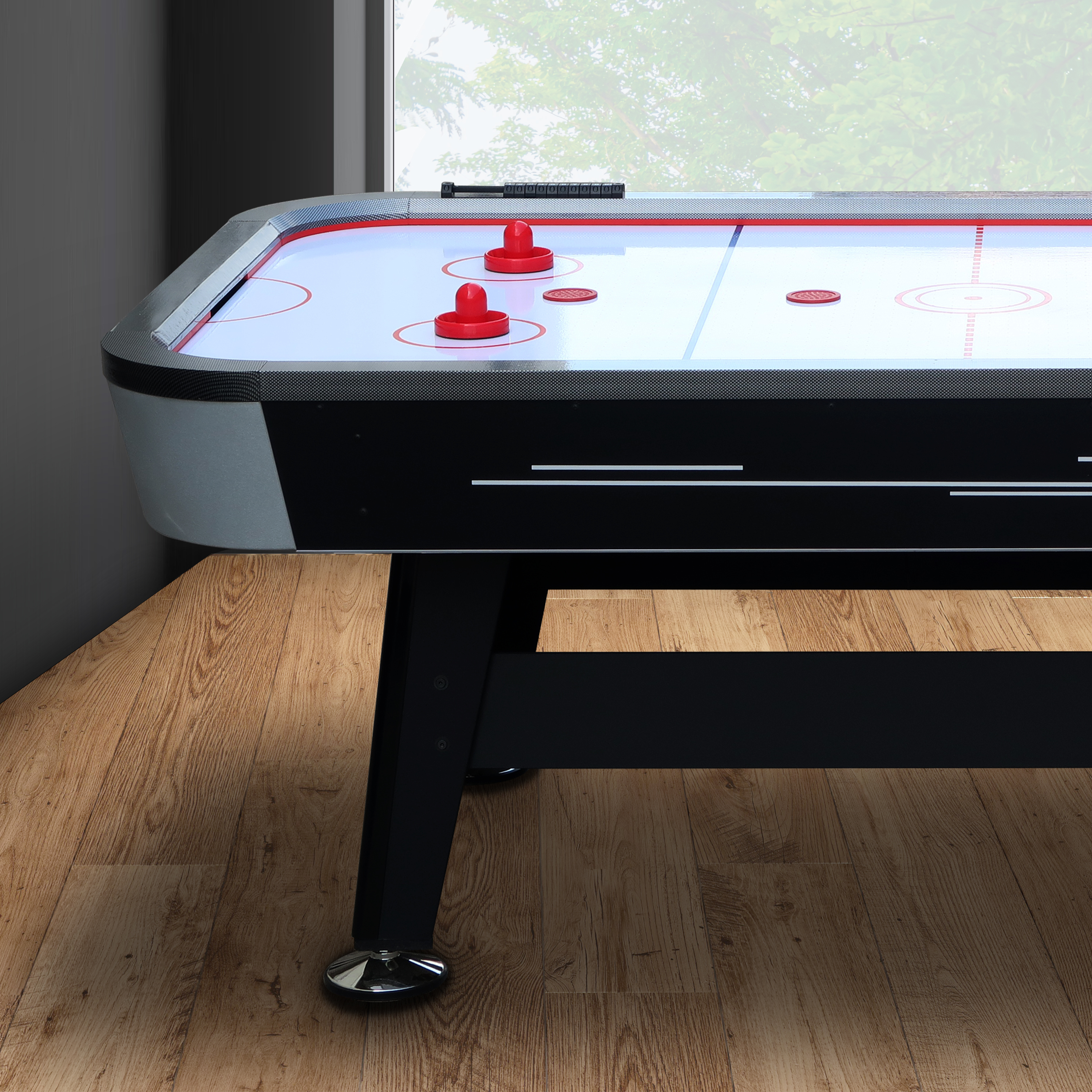 Air-Hockey-Tisch mit roten Pucks. Schwarzer Rahmen, weiße Oberfläche mit roten Linien, Holzboden.