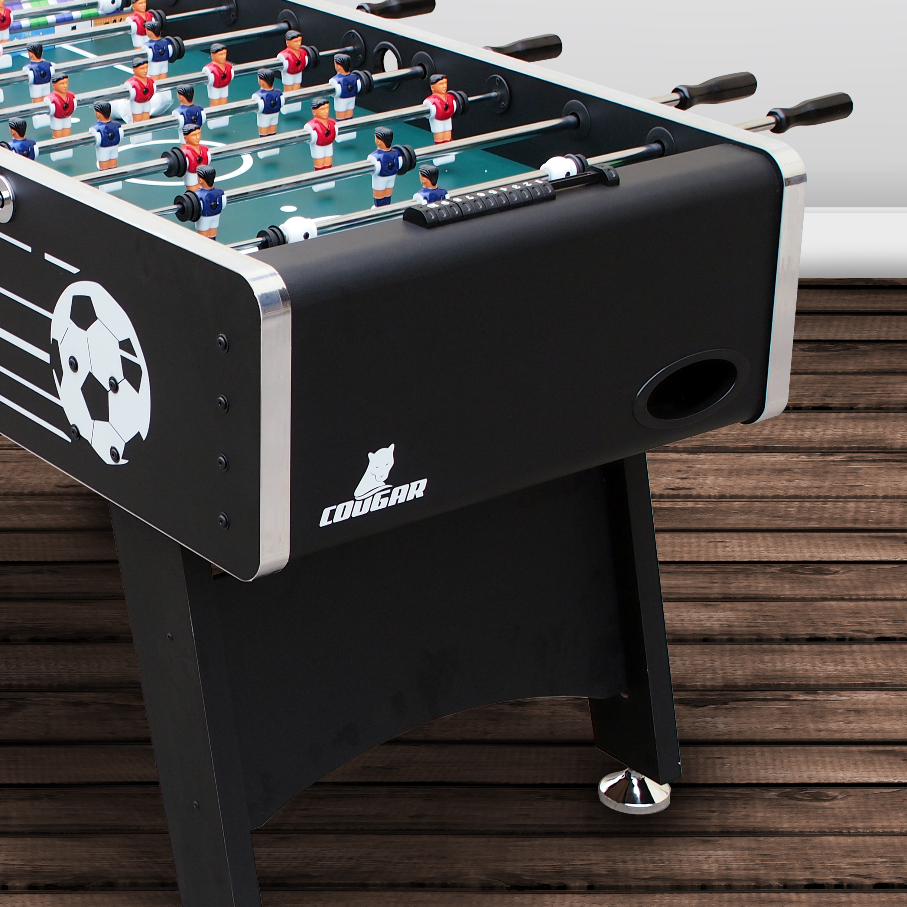 Ein Tischfußballtisch, schwarz mit Fußball und Spielern, auf einem Holzboden.