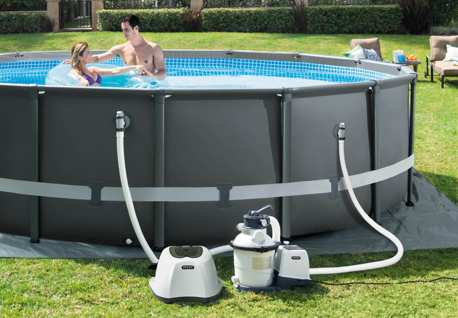 Ein Paar in einem Pool mit Filter und Pumpe. Grünes Gras und ein grauer Pool umgeben den Pool.