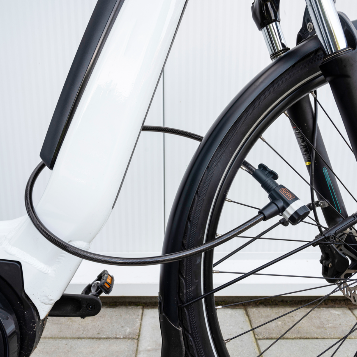 Het wiel en frame van een fiets. Een kabelslot is aan het frame bevestigd.