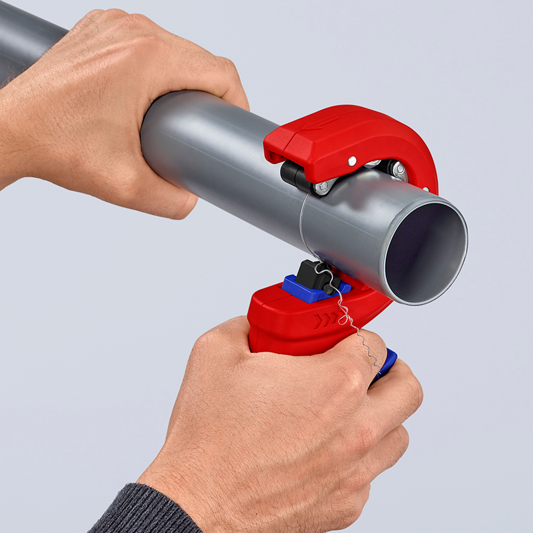 Mains utilisant un coupe-tube rouge sur un tuyau gris. Le coupe-tube est rouge et bleu.