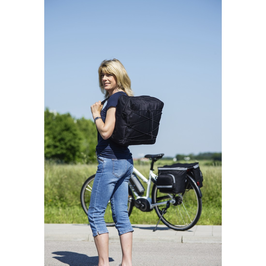 Eine Frau mit einer schwarzen Fahrradtasche schaut über ihre Schulter. Fahrrad im Hintergrund.