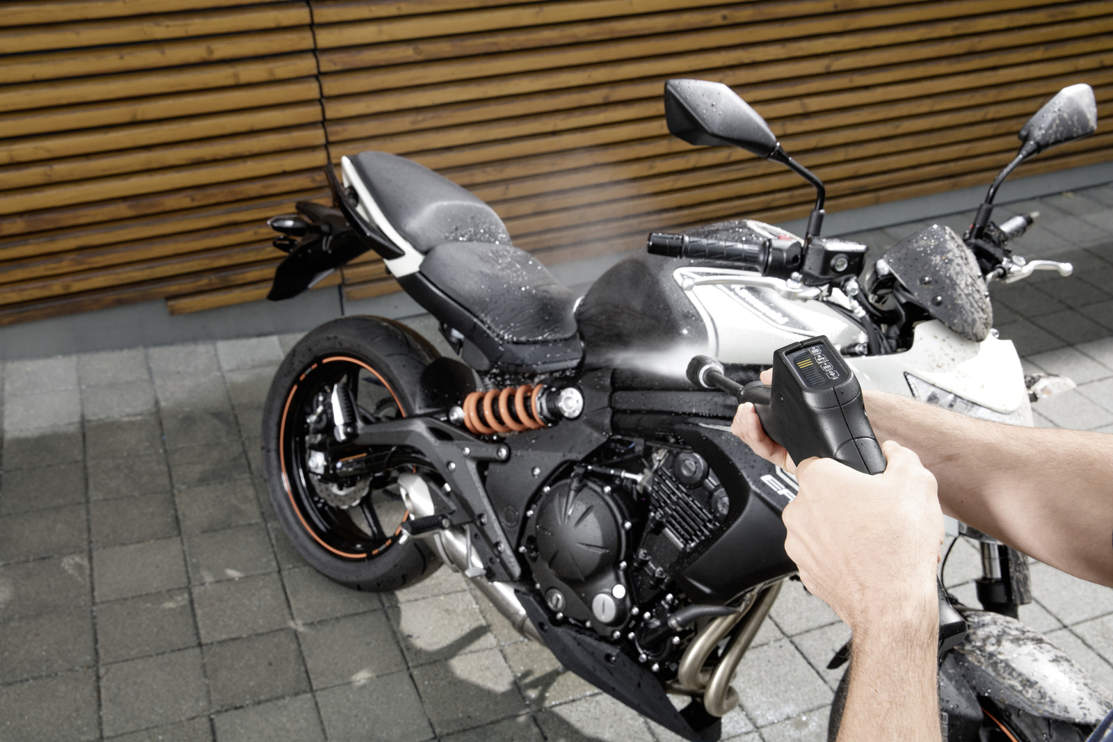Una persona pulisce una moto nera con un'idropulitrice. La moto è su una superficie di mattoni.