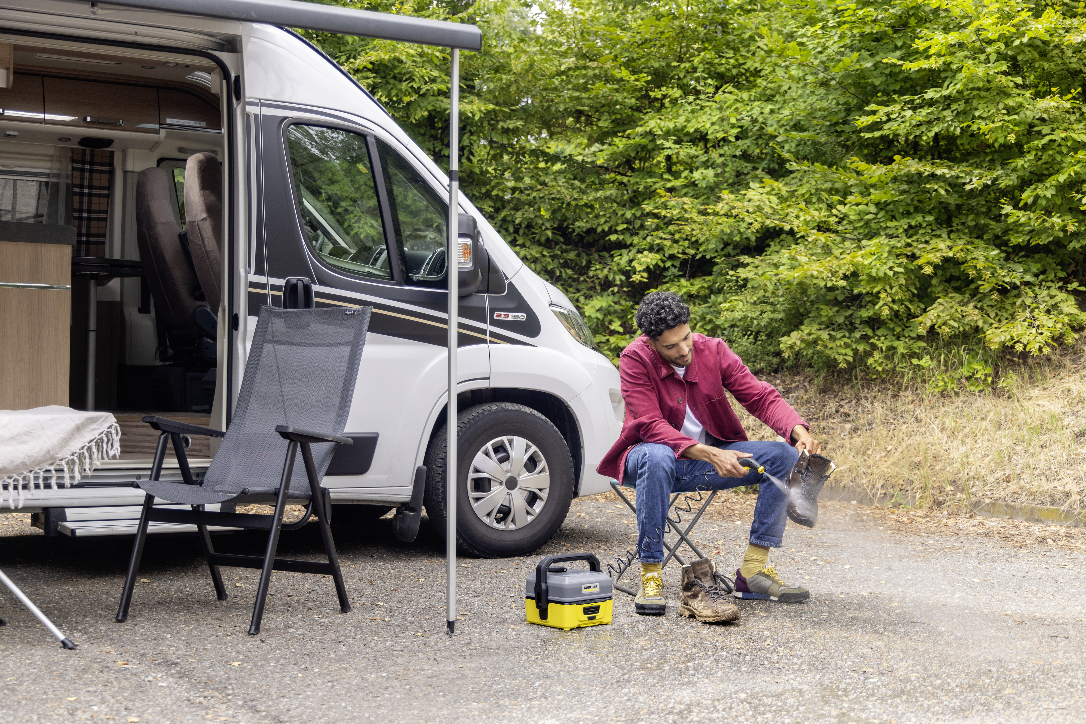 Un homme nettoyant ses bottes près d'un camping-car, avec du matériel de camping.