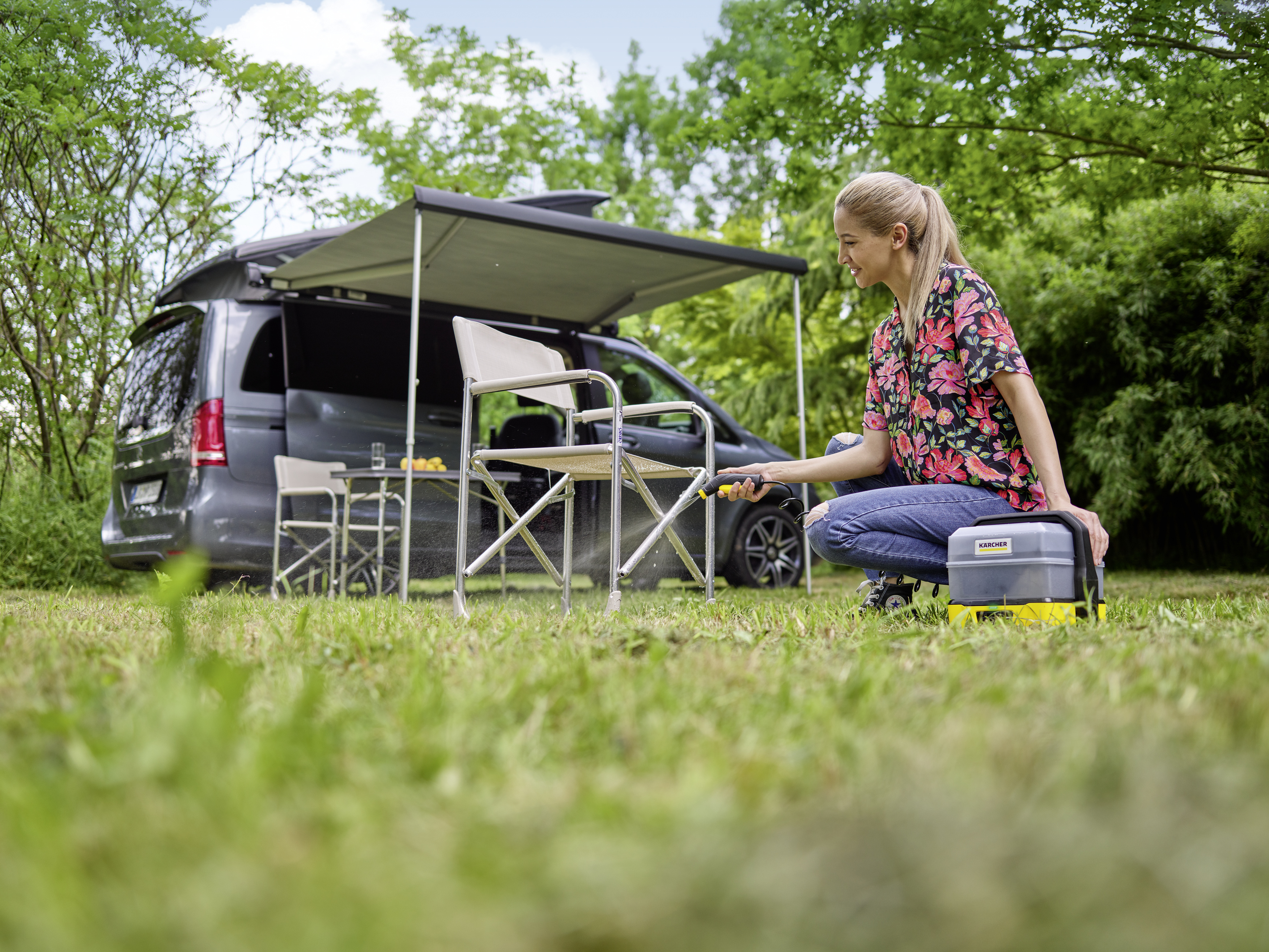 Femme agenouillée, lave voiture près d'un camping-car. Herbe verte et arbres.