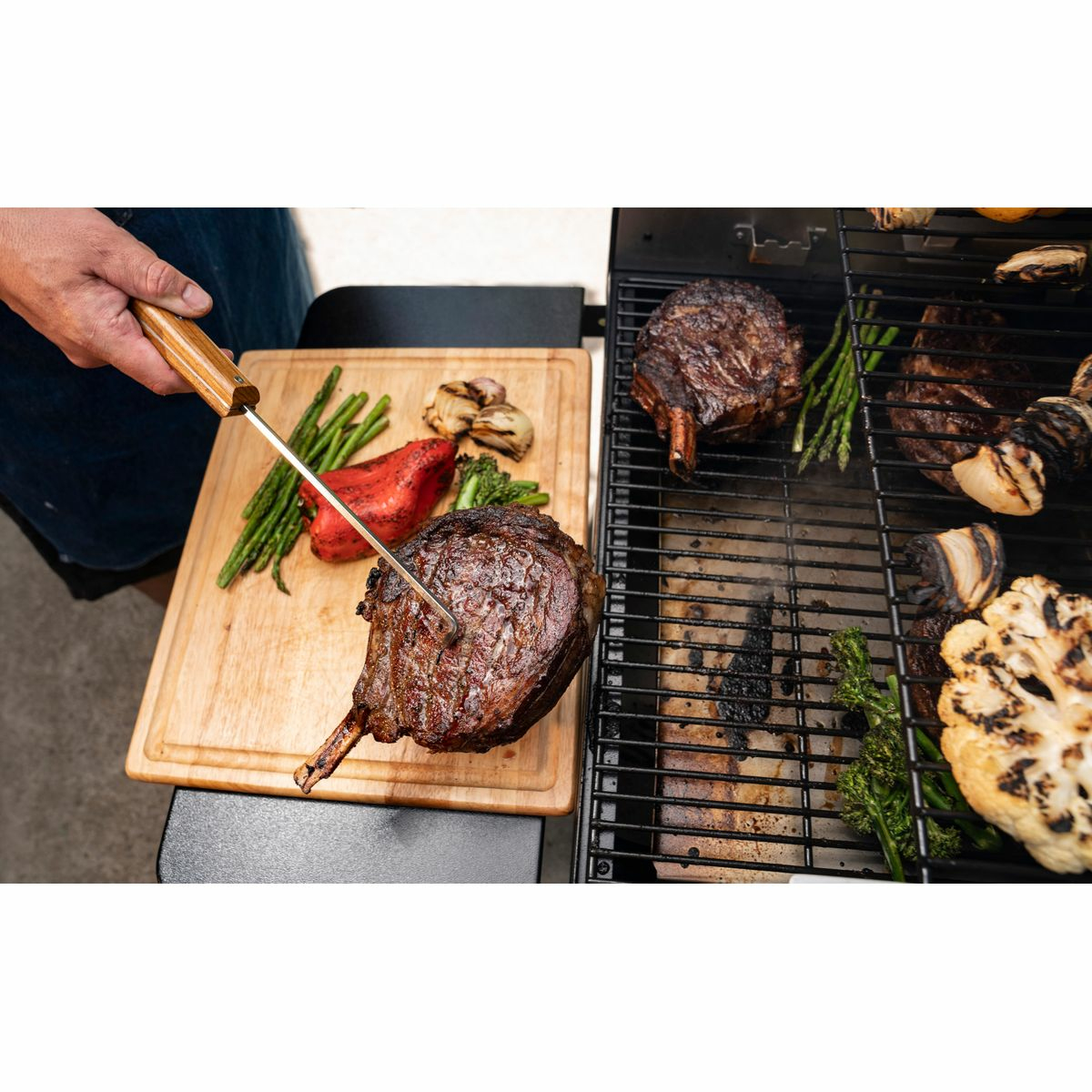 Osoba grilluje mięso i warzywa na czarnym grillu. Zawiera stek, szparagi i kalafior.