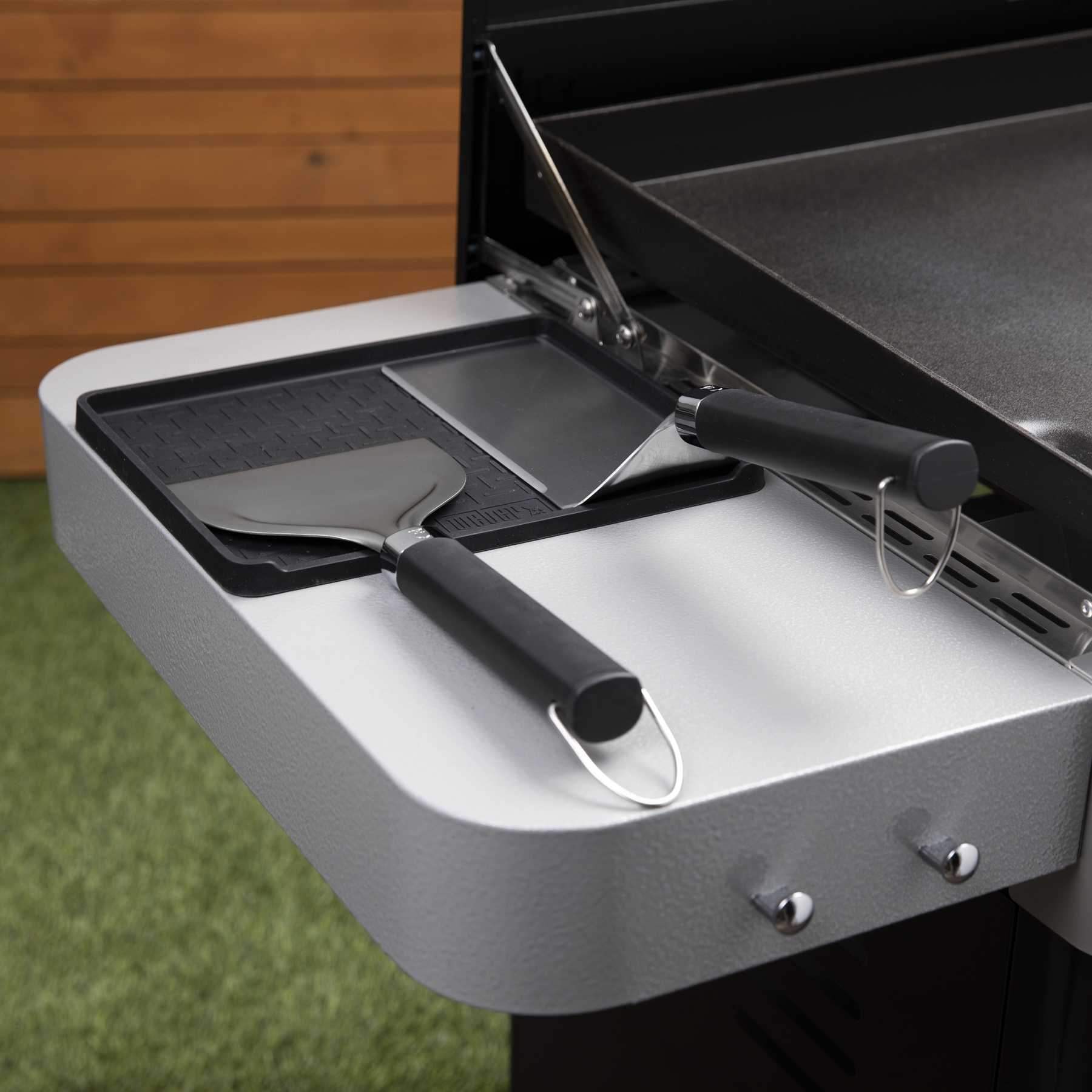 Grill z narzędziami z boku. Szpatułka i inne narzędzia znajdują się na metalowej półce.