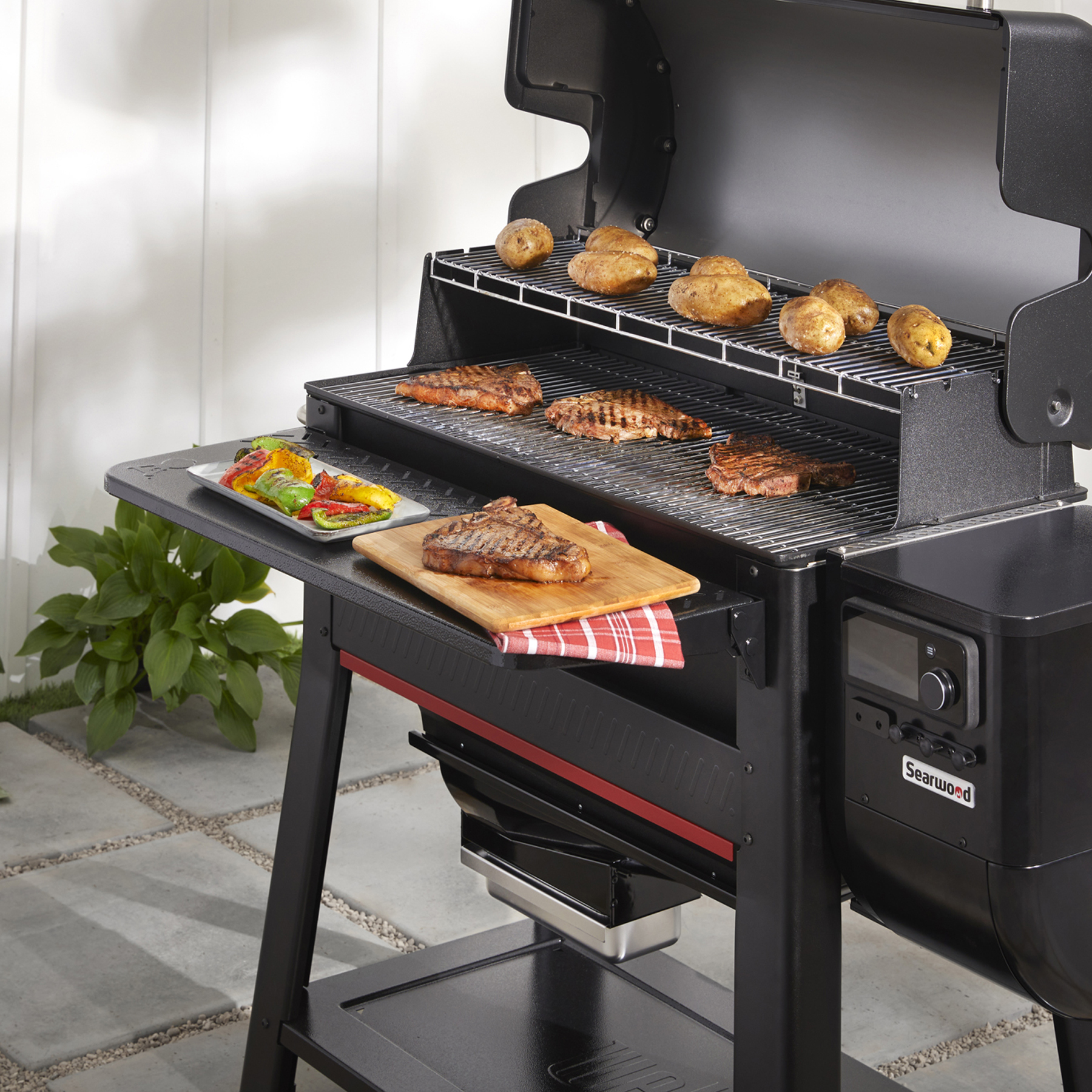 Parrilla exterior con comida cocinándose en las parrillas y una mesa lateral con comida.