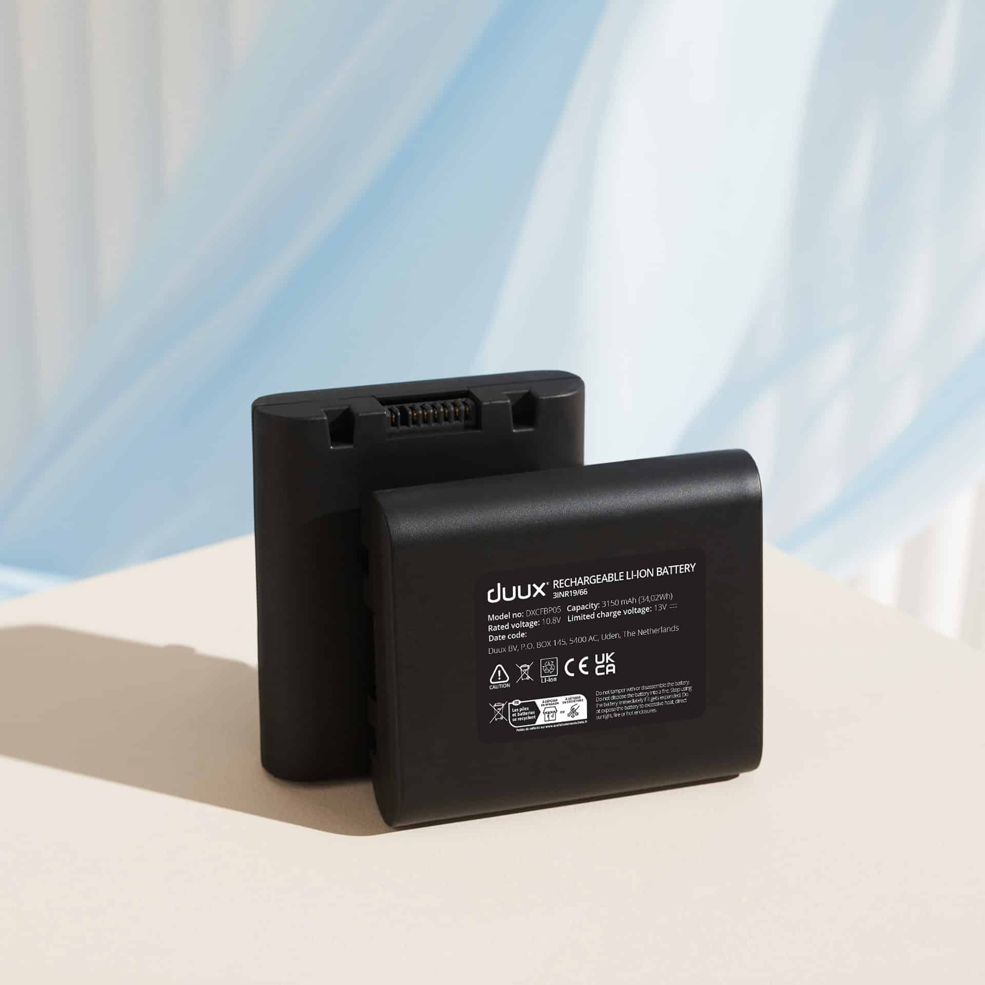 Two black rechargeable Li-ion batteries, with product information on the front, on a light surface.