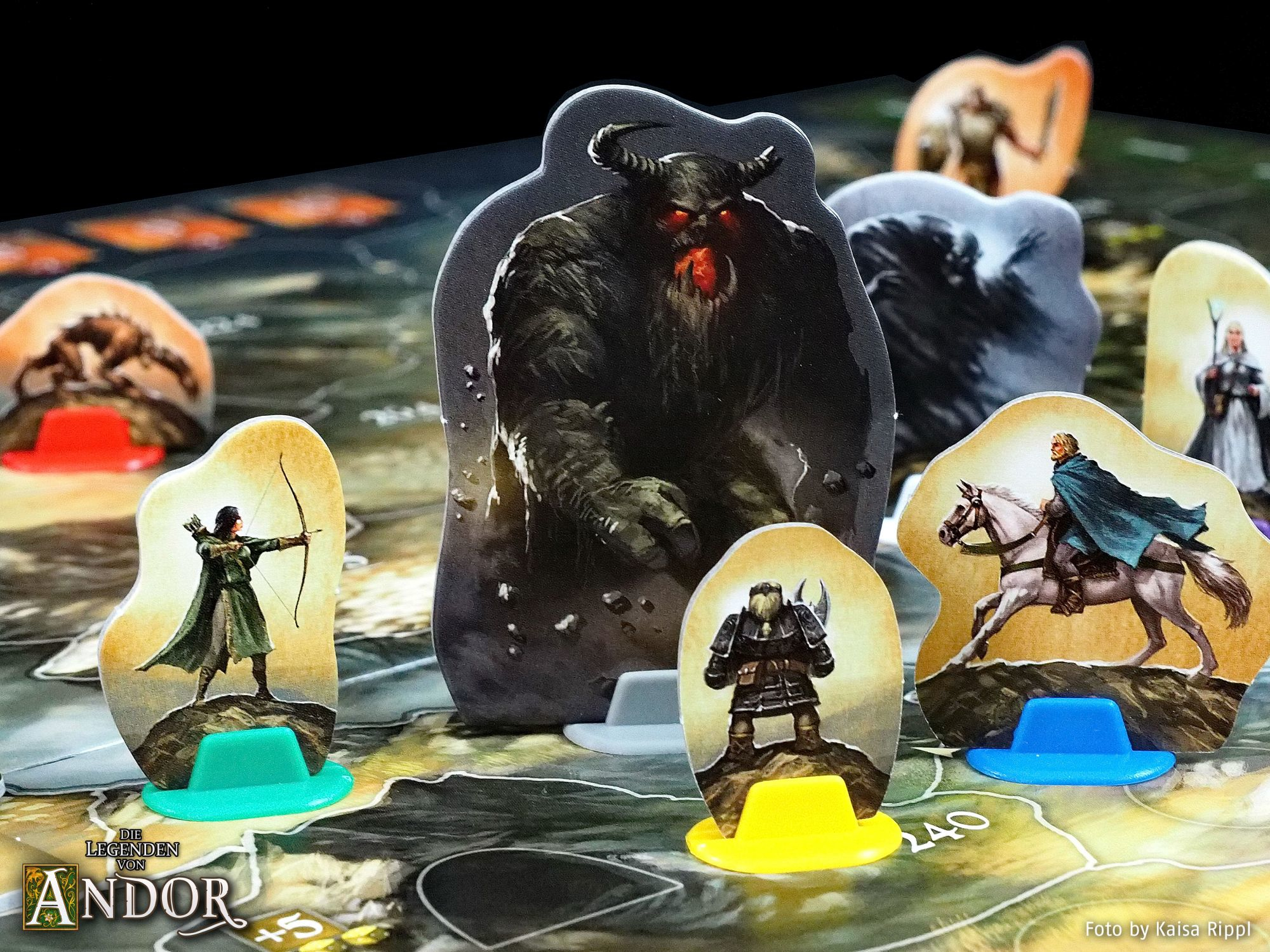 Brettspiel mit Figuren aus einer Fantasiewelt auf einem Spielbrett. Text auf Deutsch.