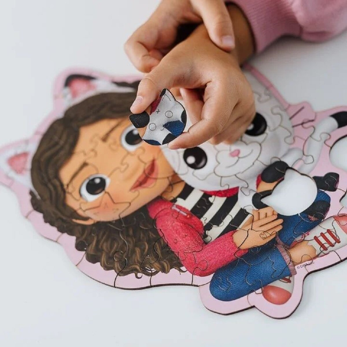 La mano de un niño sosteniendo una pieza del rompecabezas de Gabby's Dollhouse que muestra la imagen.