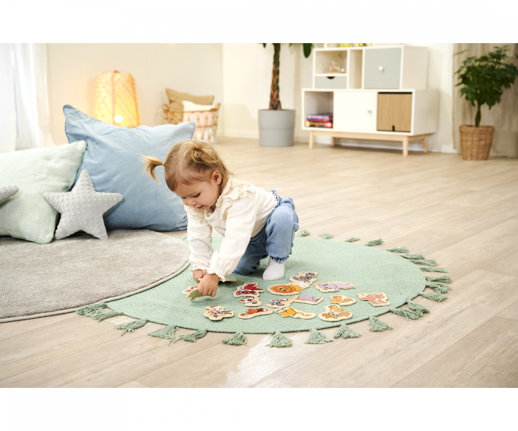 Junges Mädchen spielt mit Holzpuzzleteilen auf einem grünen Teppich.