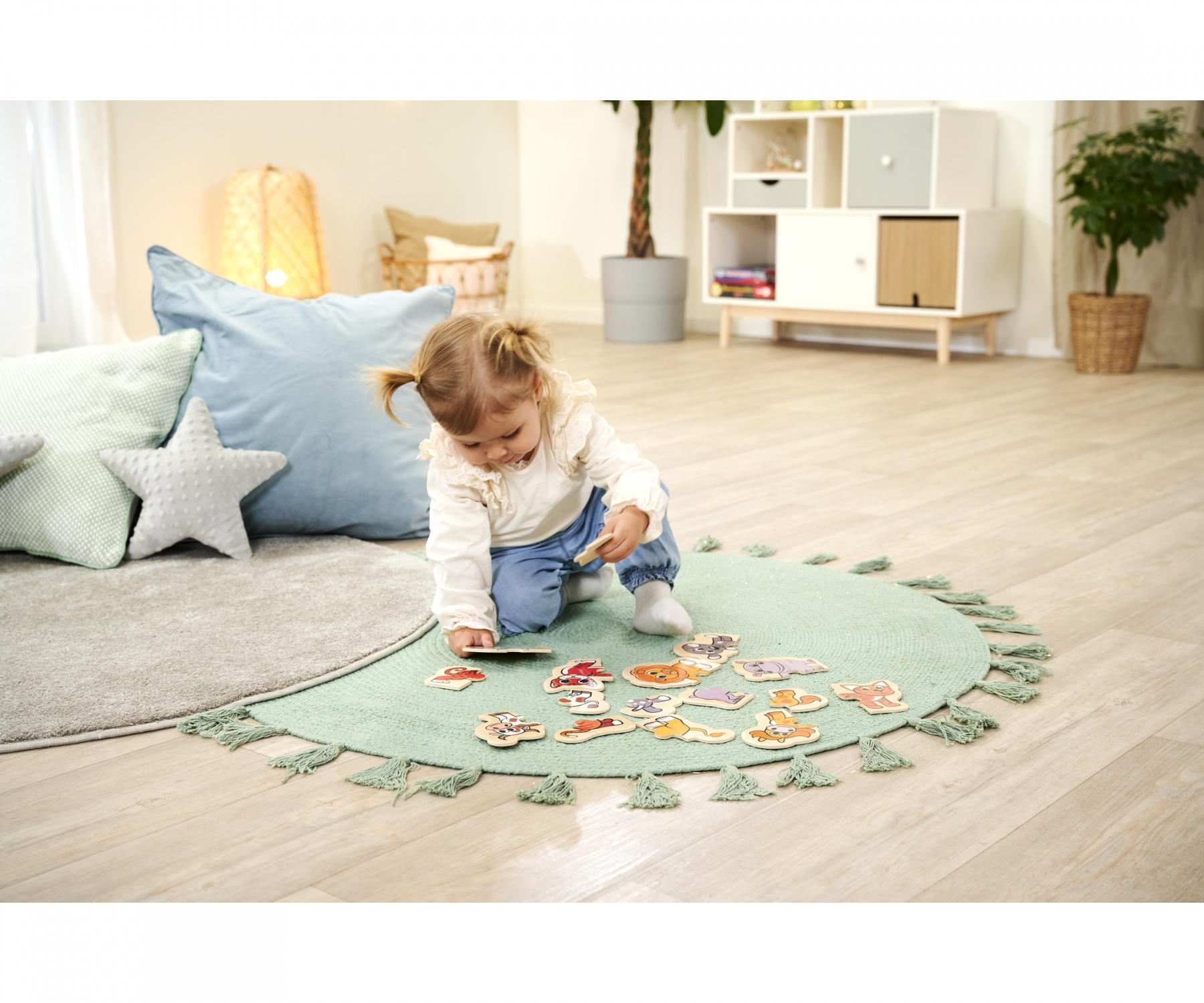 Ein junges Kind spielt mit Holzpuzzleteilen von Tieren auf einem runden Teppich mit Quasten.