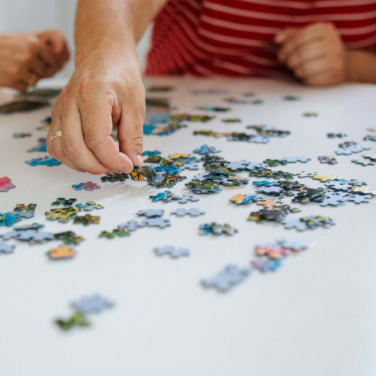 Ręce układające puzzle na białej powierzchni, z umieszczonymi elementami.