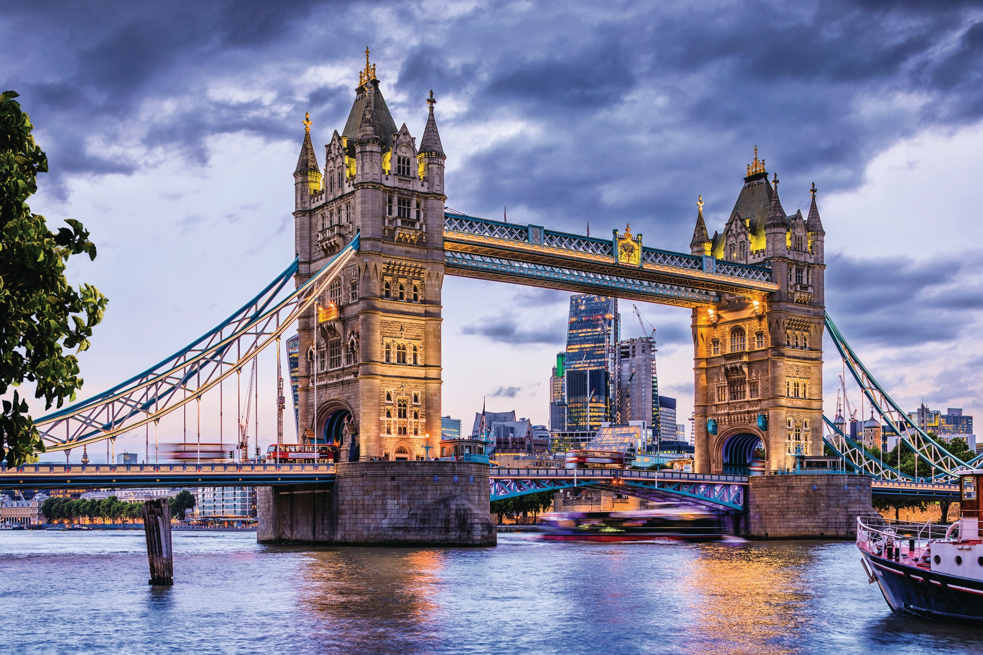 Tower Bridge in London bei Dämmerung, mit Lichtern und Booten auf dem Wasser.