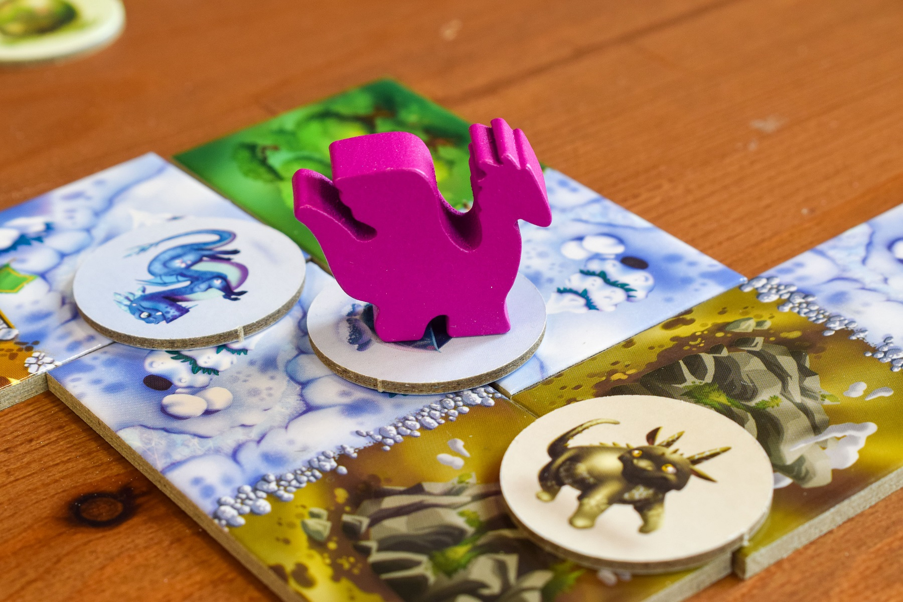 Elementy gry planszowej na kolorowych kafelkach. Różowy smok i pionek na białym okręgu.