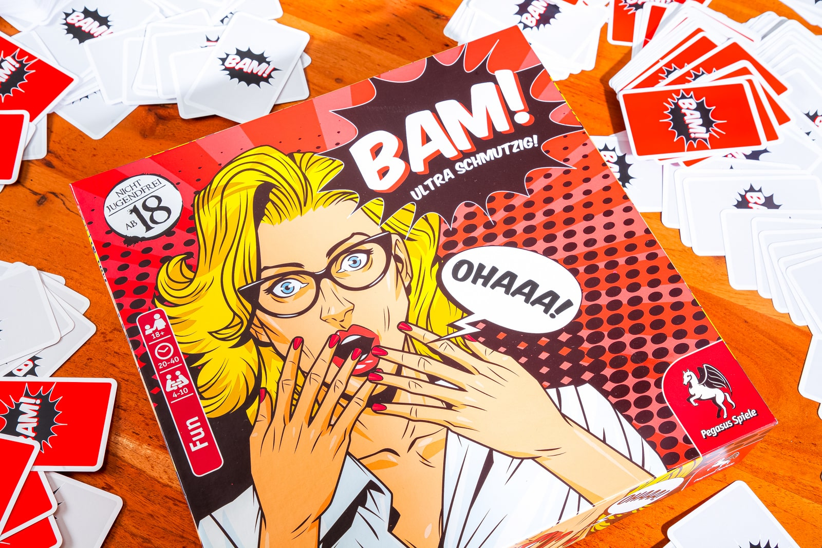 Pudełko gry planszowej z twarzą kobiety w stylu komiksowym, otoczone kartami, z tytułem 'BAM!'