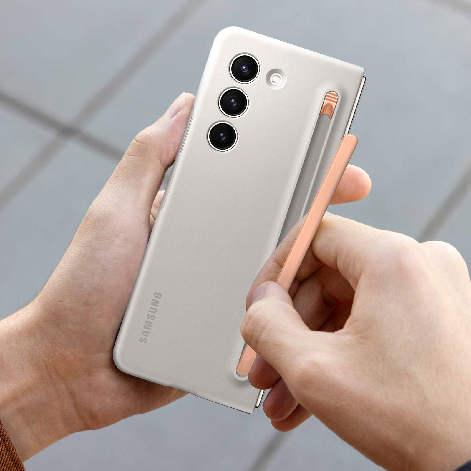 Mani che tengono un telefono grigio con uno stilo. Il telefono ha tre fotocamere e il logo Samsung.