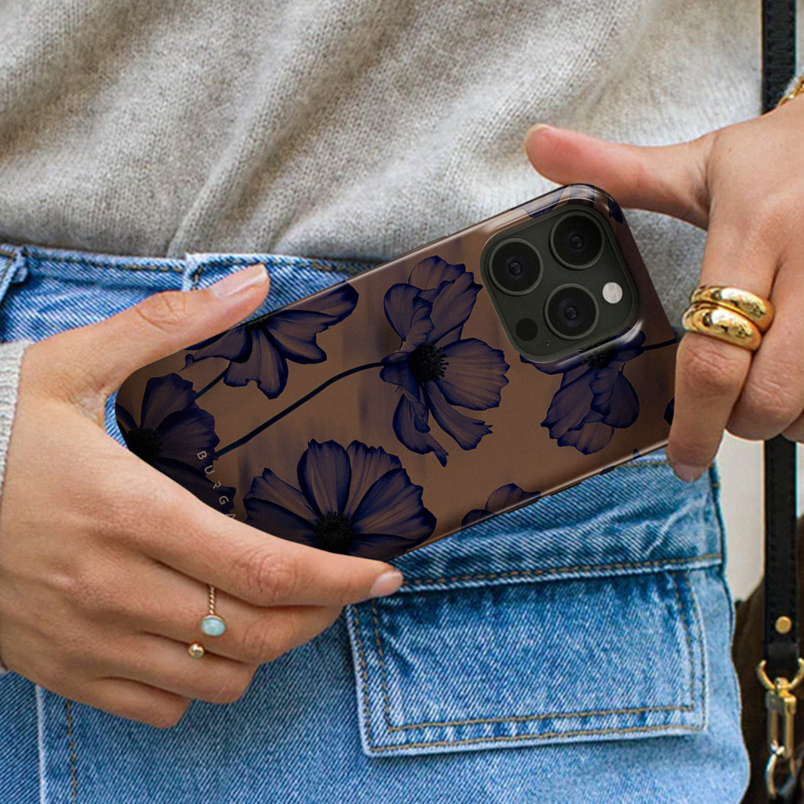 Donna che tiene una custodia per telefono con design a fiori blu. Indossa jeans e un maglione grigio chiaro.