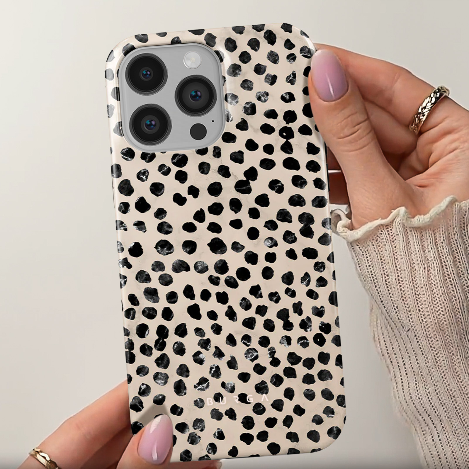 Una mano tiene una custodia per telefono con macchie nere su uno sfondo beige. La custodia ha lenti della fotocamera.