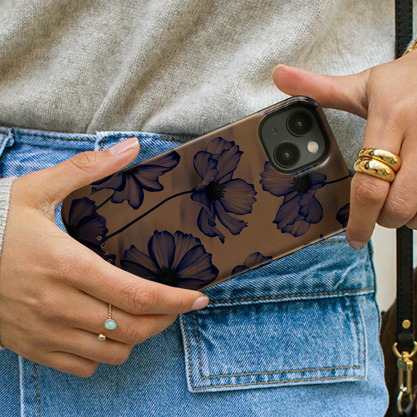 Een vrouw houdt een telefoonhoesje vast met een bloemenontwerp. De hoes heeft blauwe bloemen op een bruine achtergrond.
