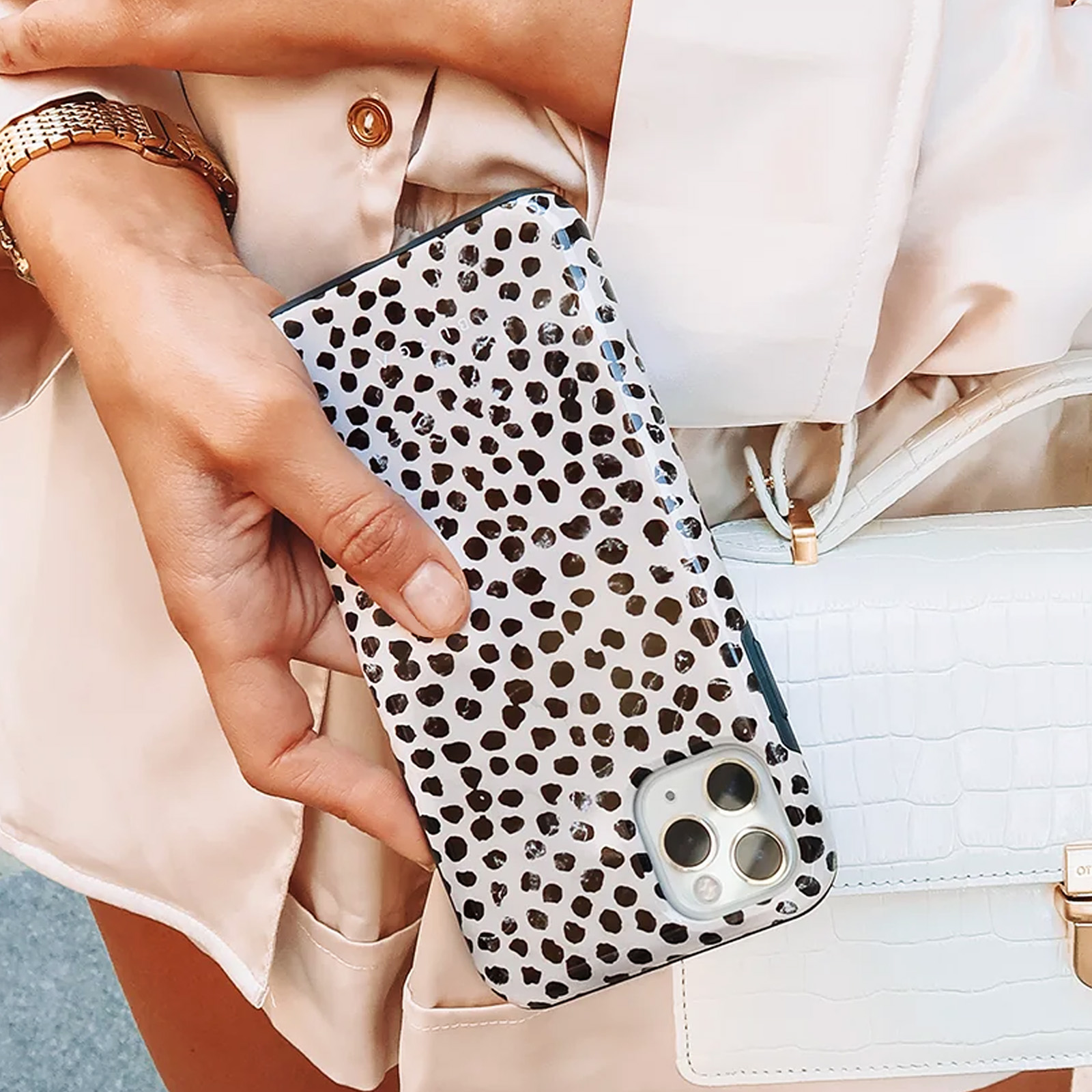 Una mano che tiene una custodia per telefono con un design a pois bianchi e neri, accanto a una borsa bianca.