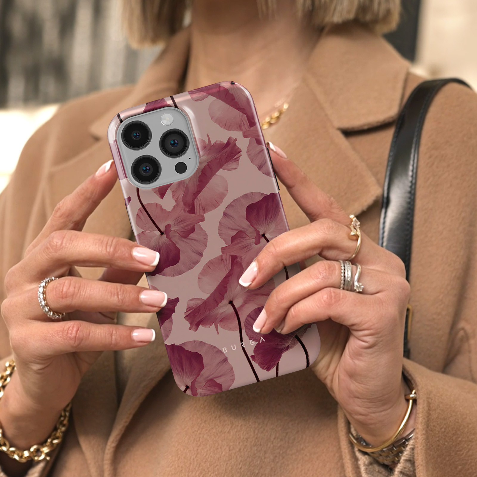 Una persona tiene in mano una custodia per telefono con un motivo floreale. La custodia presenta fiori rosa e il marchio BURGA.