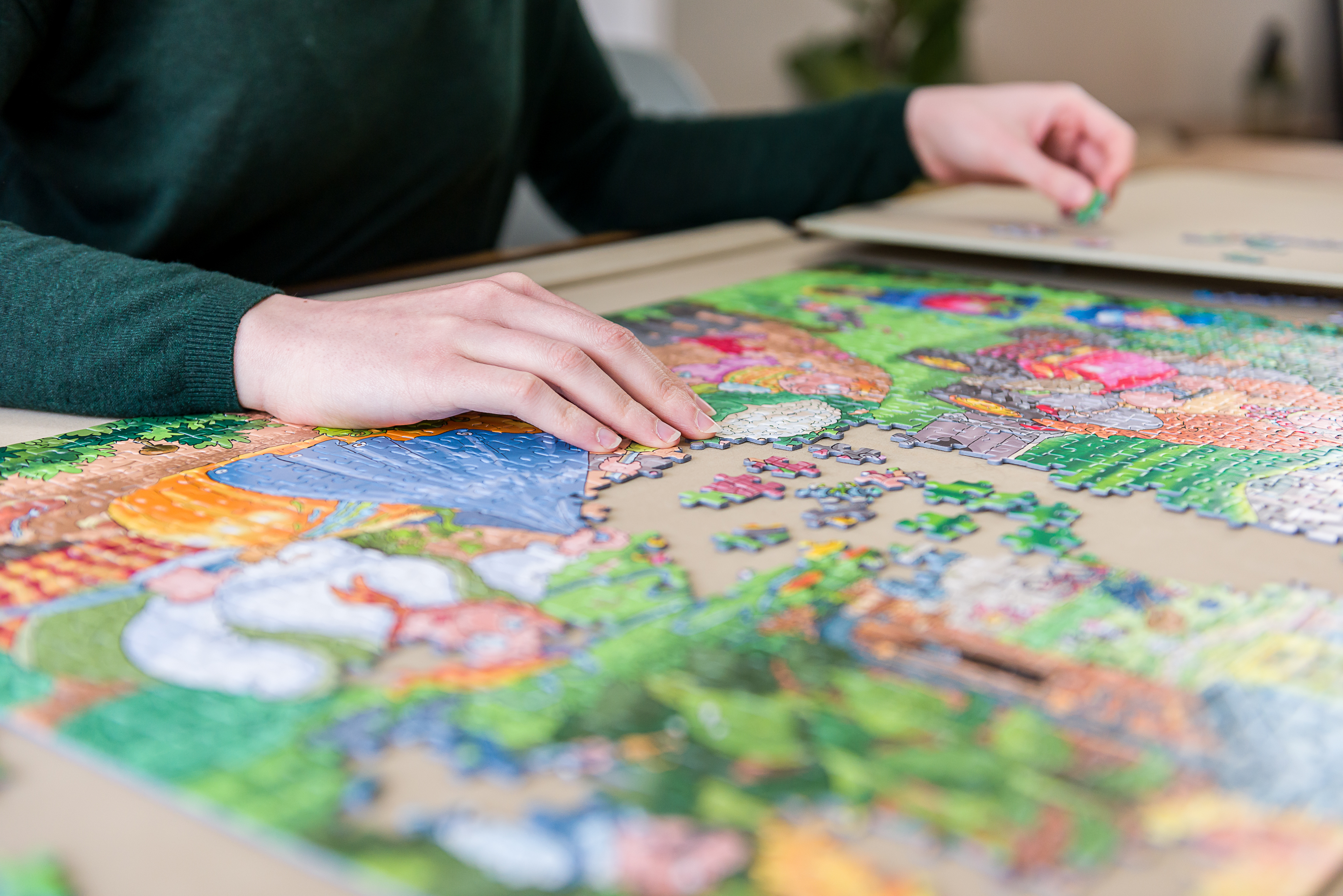 Hands of a person assembling a jigsaw puzzle, with pieces scattered on the table.