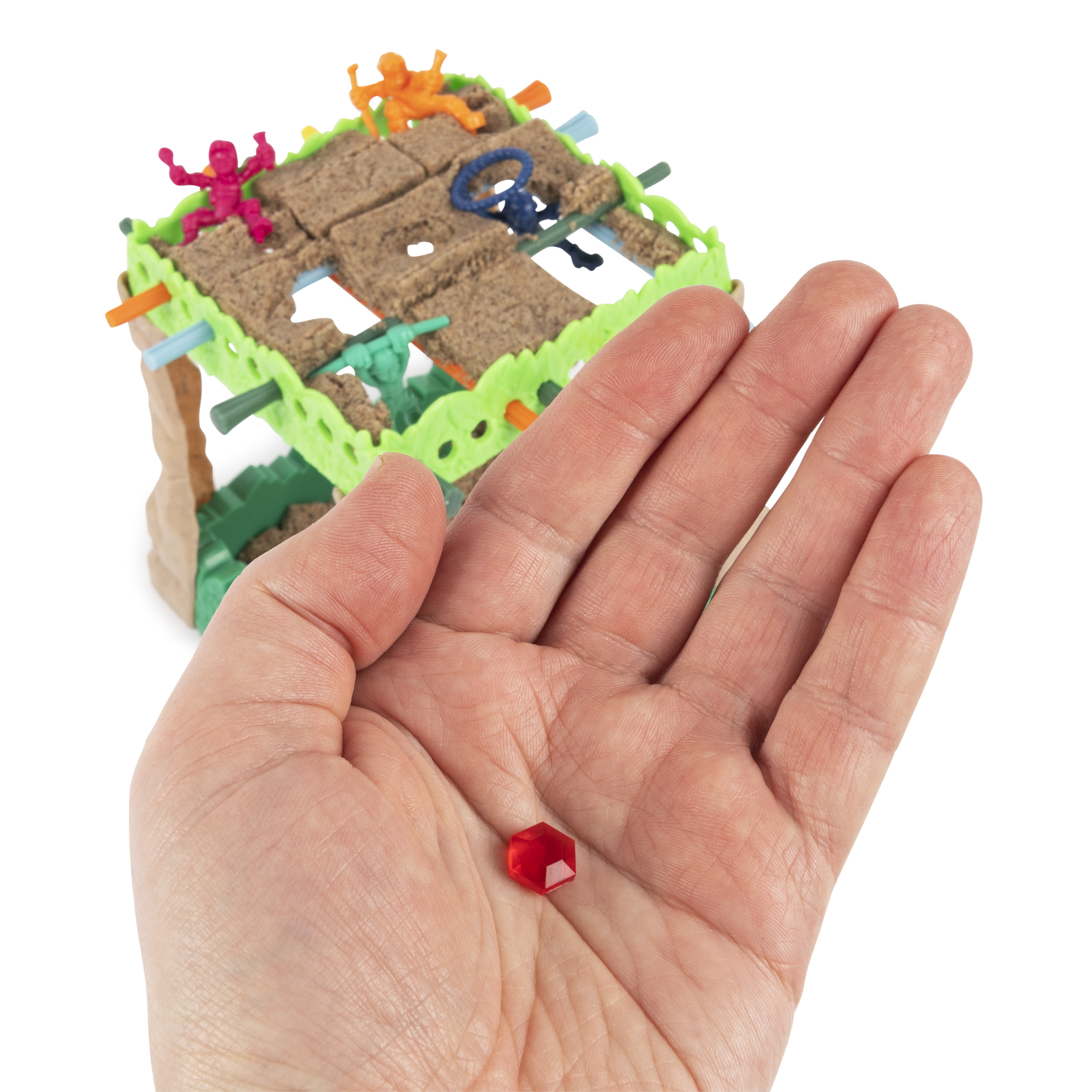 Hand hält einen roten Edelstein vor einem Miniaturspiel. Das Spiel ist grün.