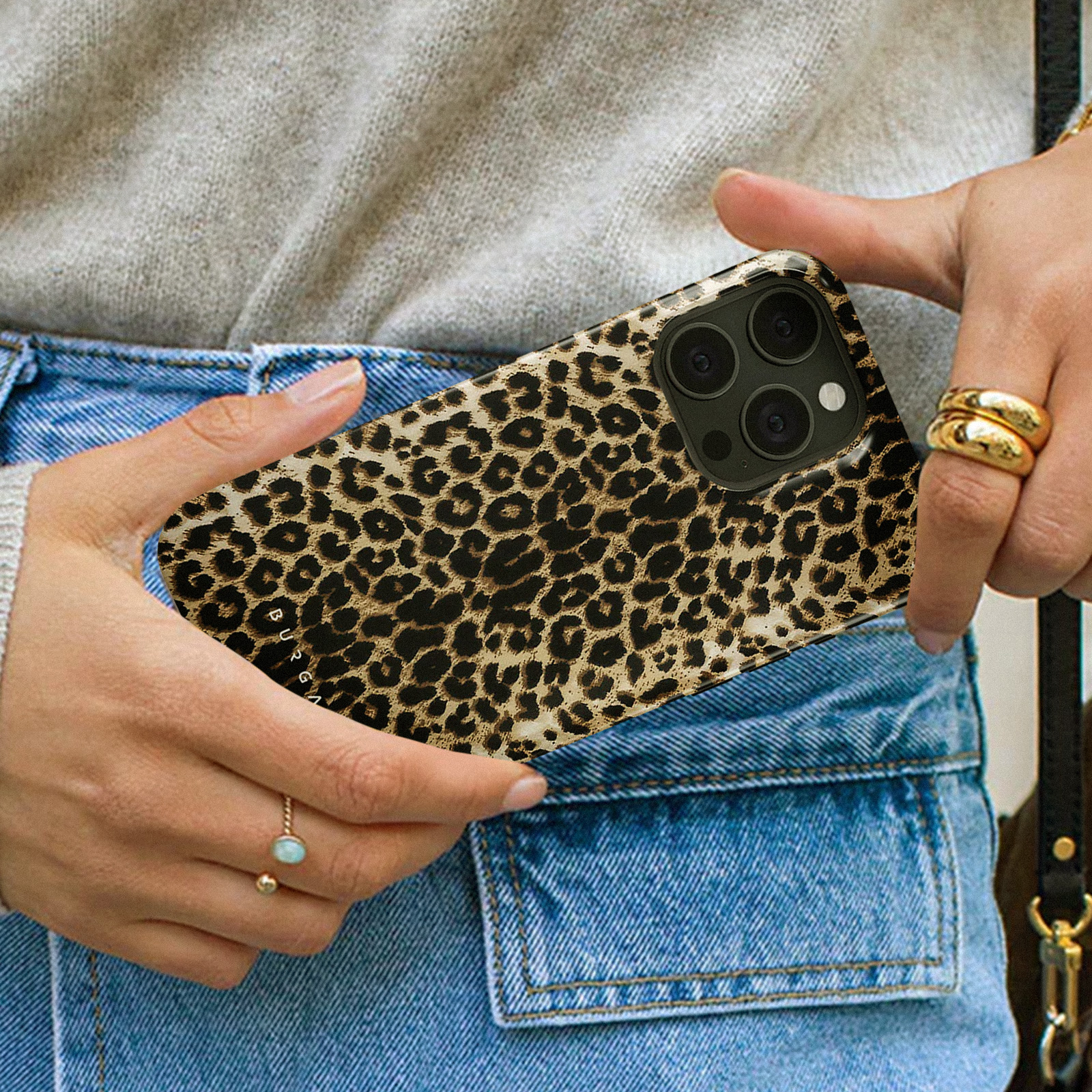 Une personne tenant une coque de téléphone à imprimé léopard avec une bosse de caméra noire et des bagues dorées.