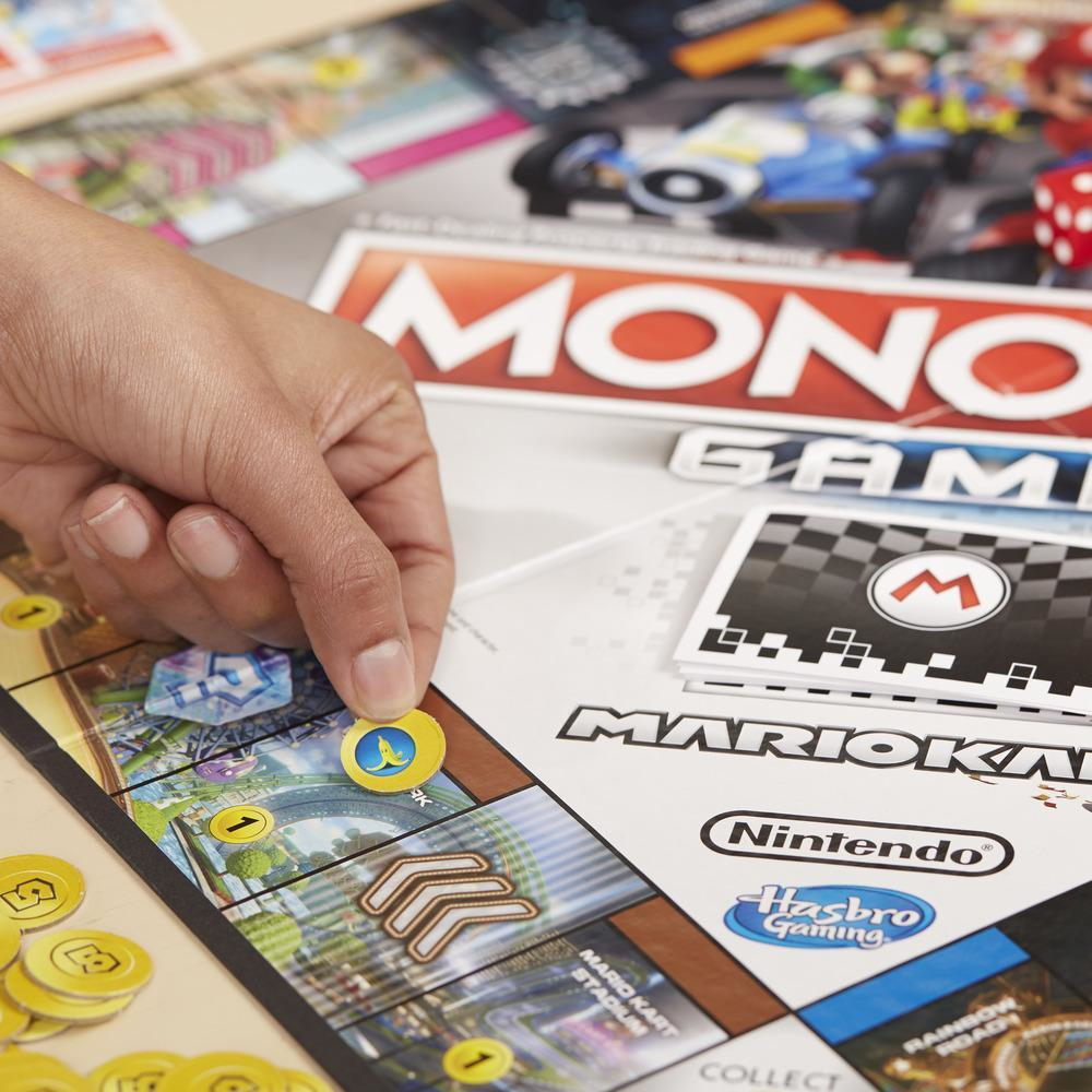 Hand, die einen Spielstein auf ein Monopoly-Spielbrett legt. Mario Kart-Thema, Würfel und Spielkarten sichtbar.