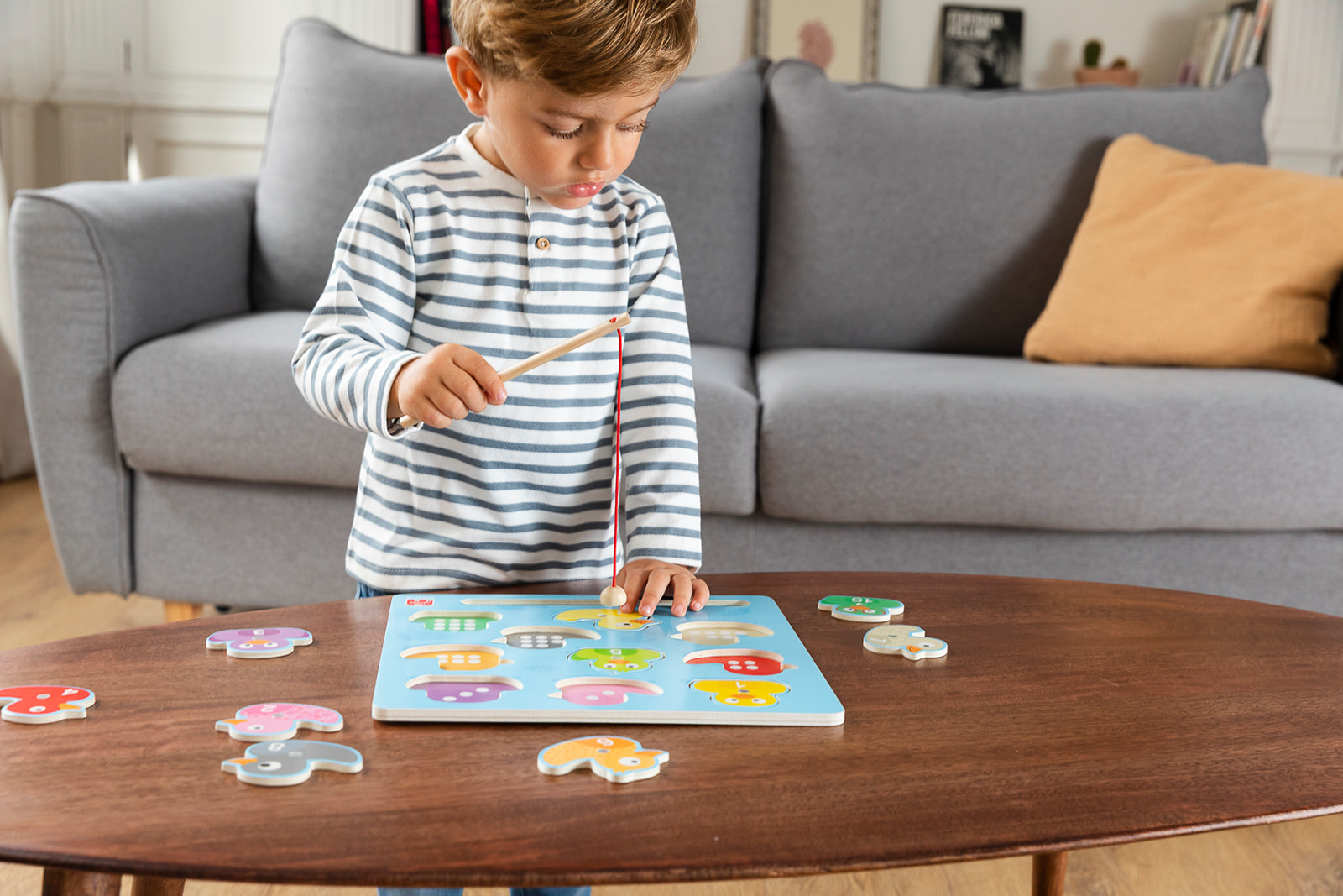 Chłopiec grający w grę wędkarską na drewnianym stole. Drewniana układanka i sofa w tle.