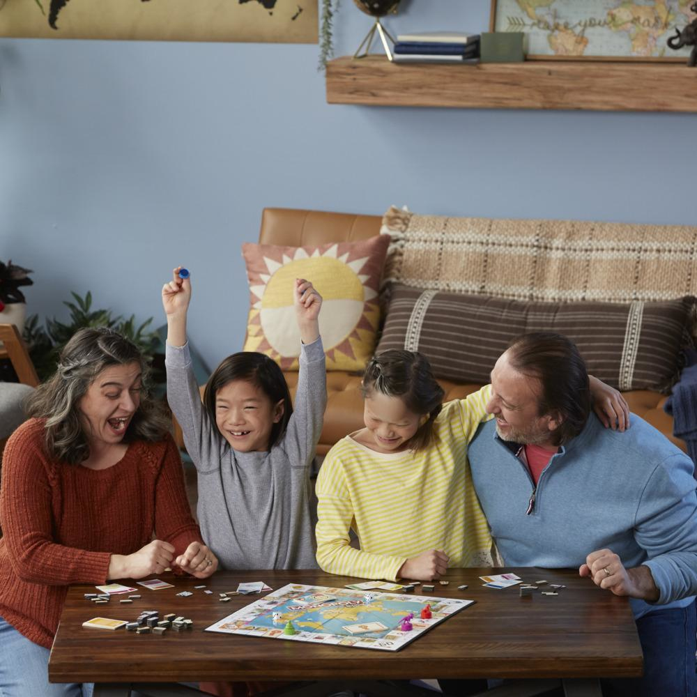 Eine Familie spielt ein Brettspiel am Tisch. Ein Kind hebt die Arme zum Sieg.
