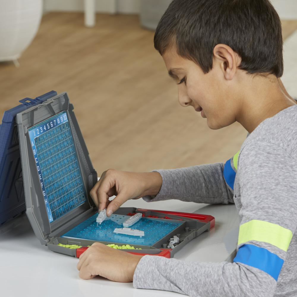 Un niño juega al Batalla Naval, colocando barcos blancos en un tablero azul. Está concentrado en el juego.