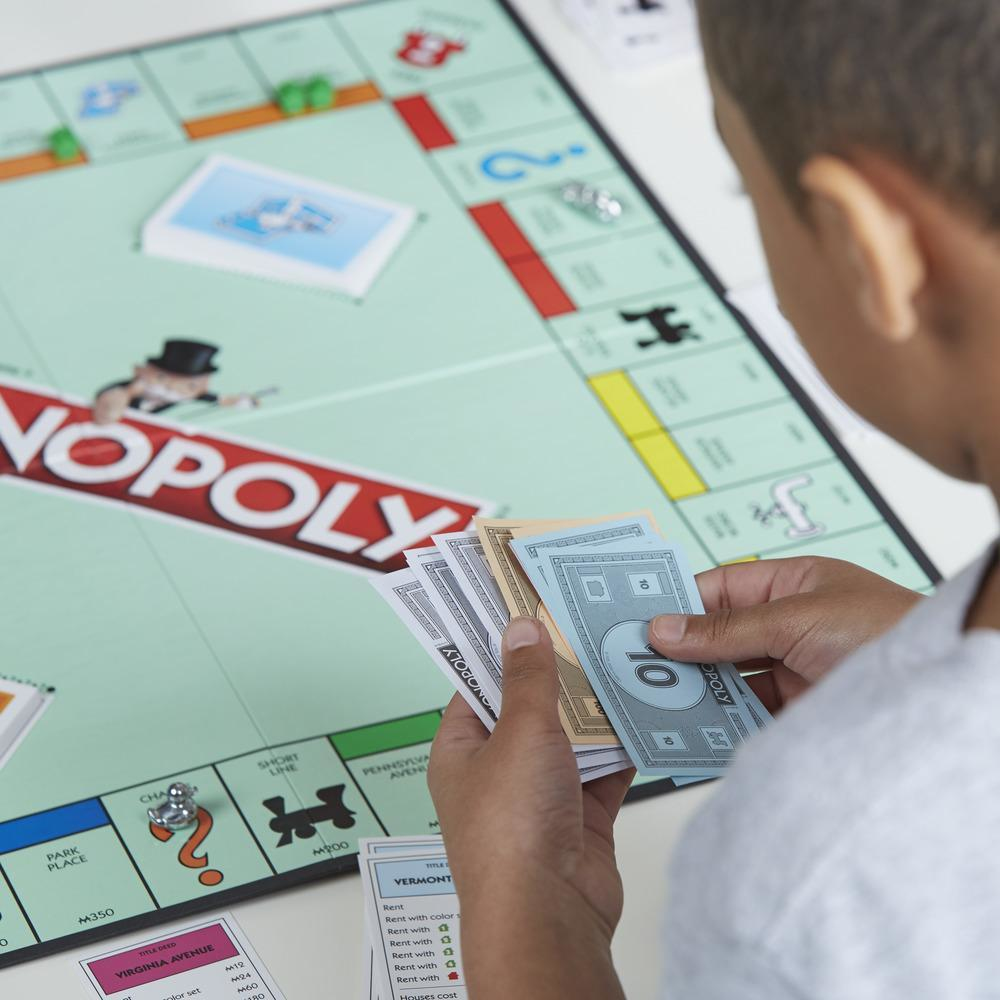 Osoba trzyma pieniądze Monopoly nad grą planszową Monopoly.