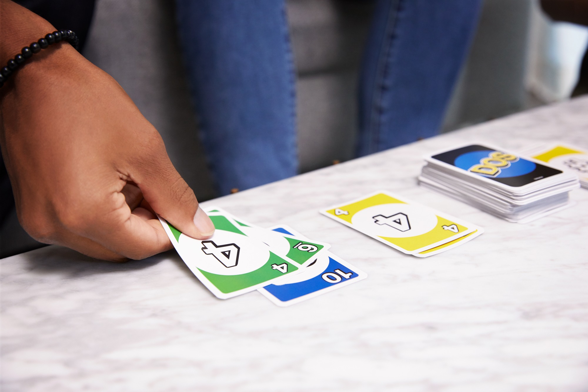 Eine Person spielt Karten, wobei die grünen und blauen Karten im Fokus stehen. Das Spiel scheint UNO zu sein.