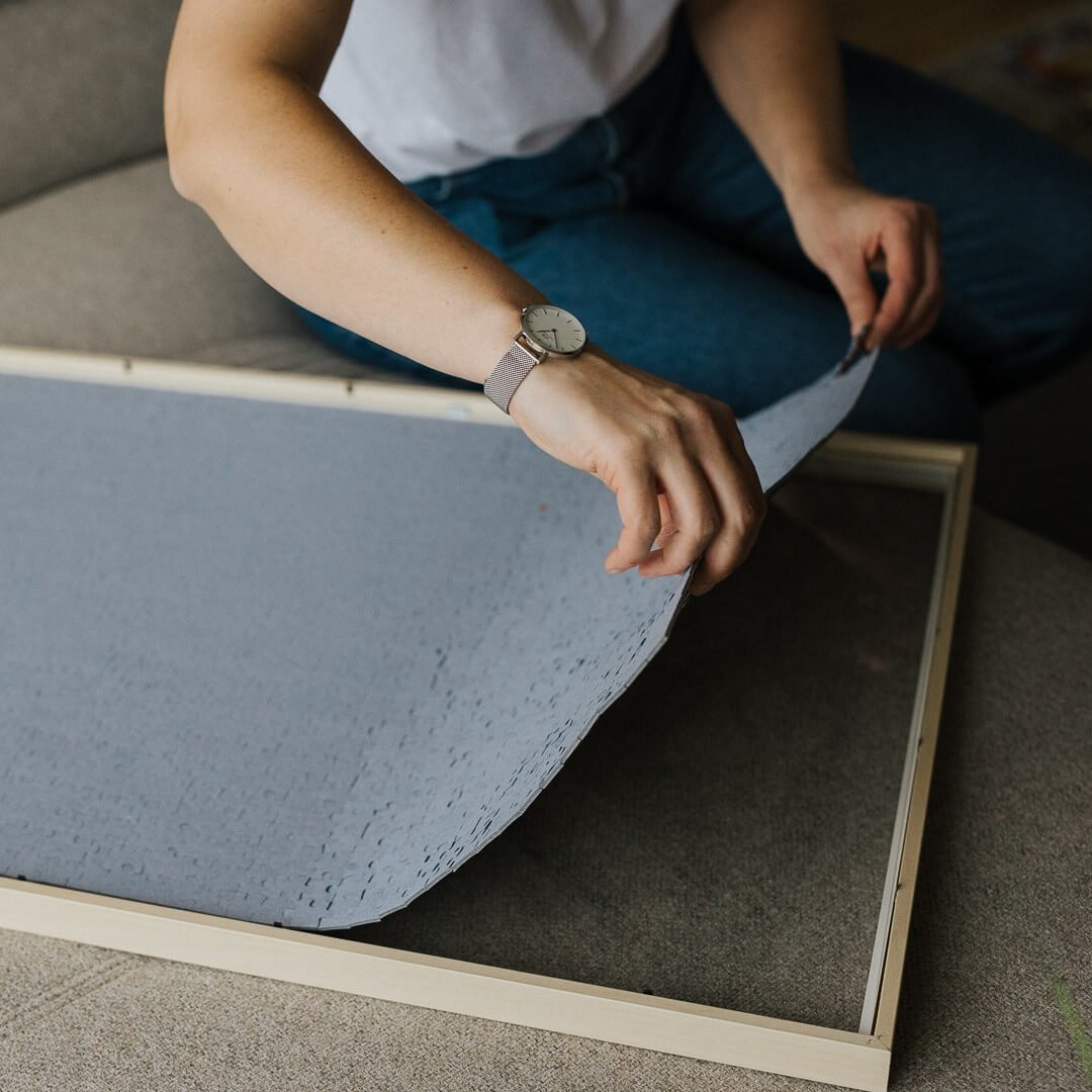 Hände einer Person platzieren ein Puzzle auf einem Holzrahmen, Nahaufnahme.