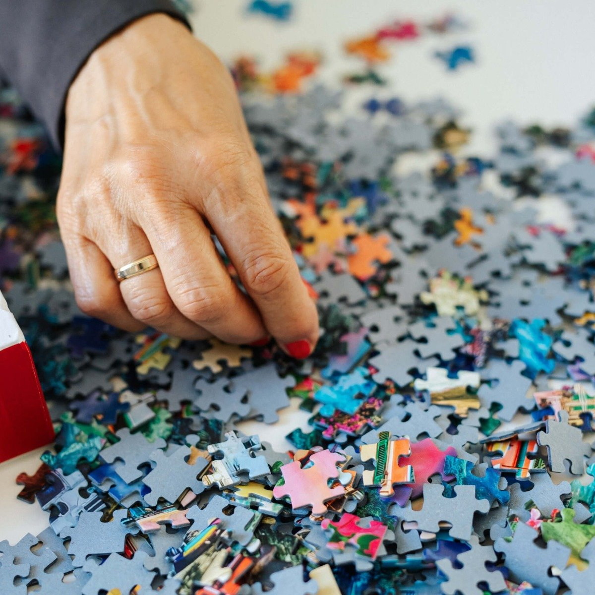 Dłoń osoby z pierścionkiem układa puzzle. Wiele elementów jest rozłożonych.