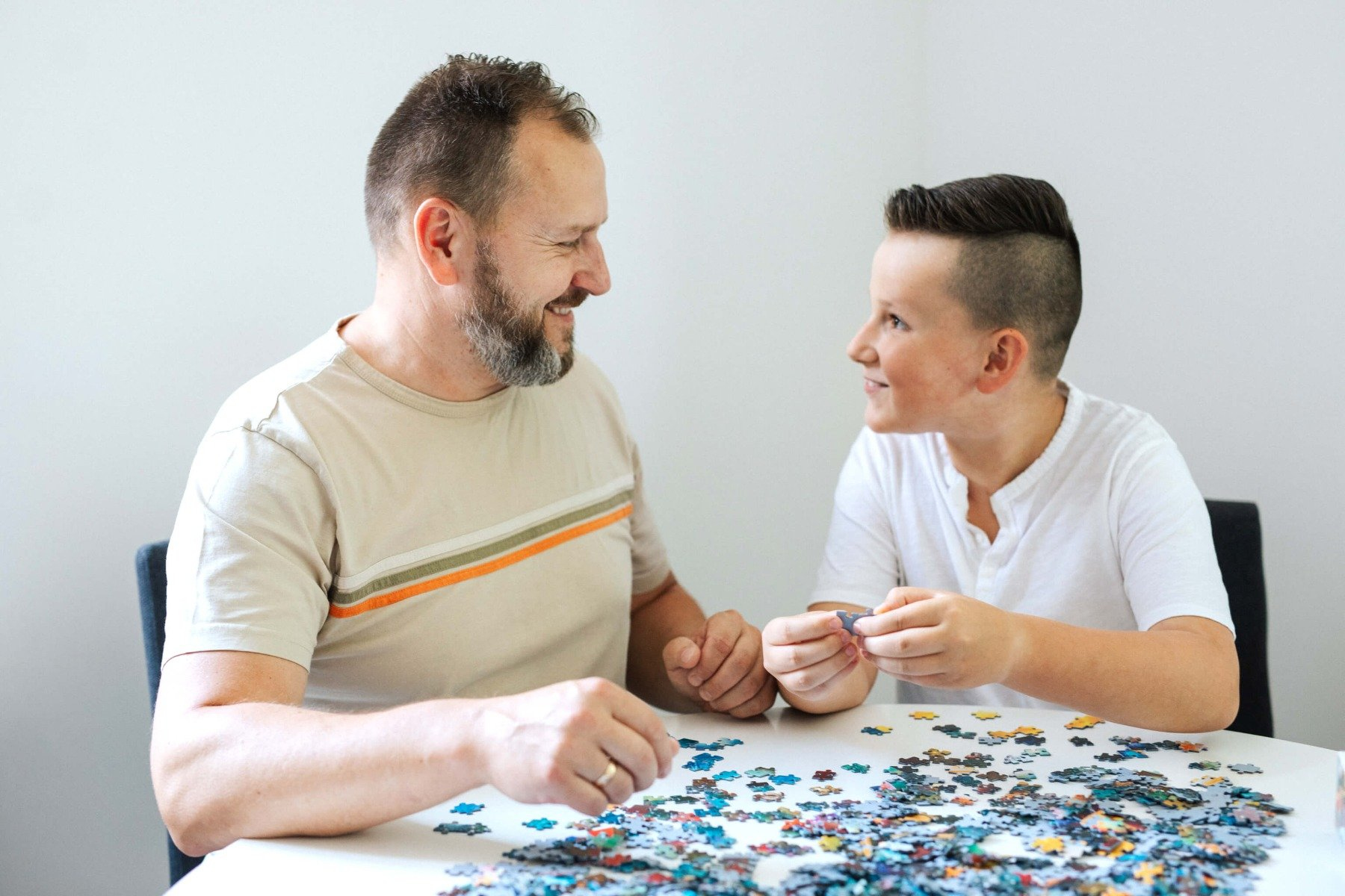 Ojciec i syn uśmiechają się, układając razem puzzle przy stole.