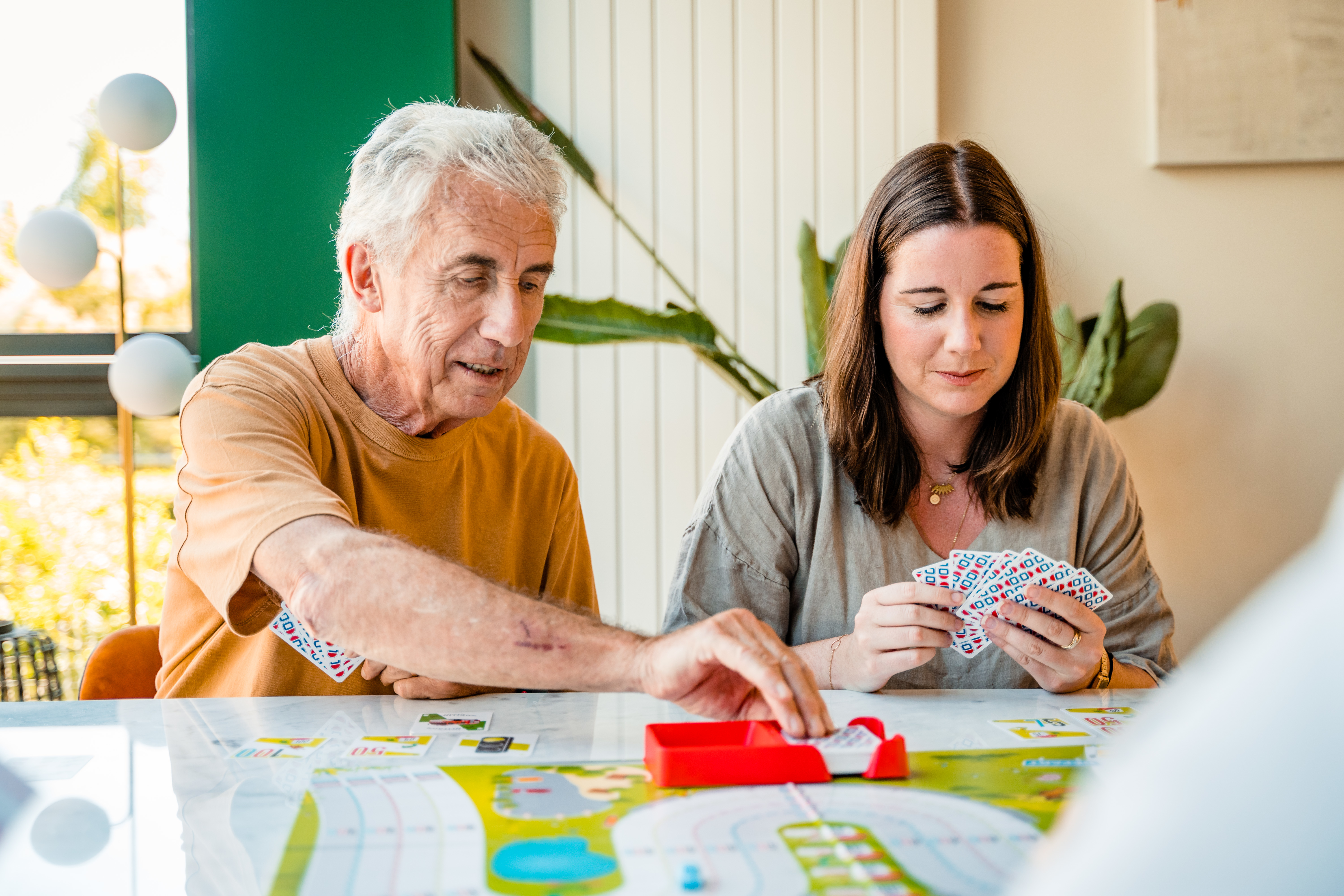 An elderly man and a woman are playing cards. Cards on the table. Green and white background.