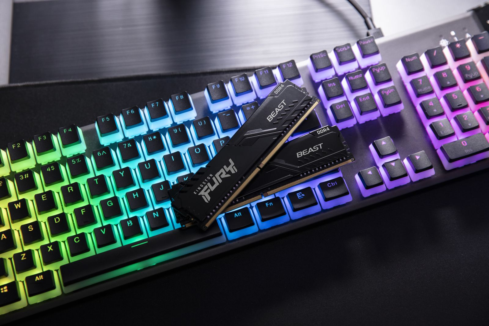 Czarne kości RAM na podświetlanej tęczowo klawiaturze. Kości mają napis Kingston FURY BEAST.