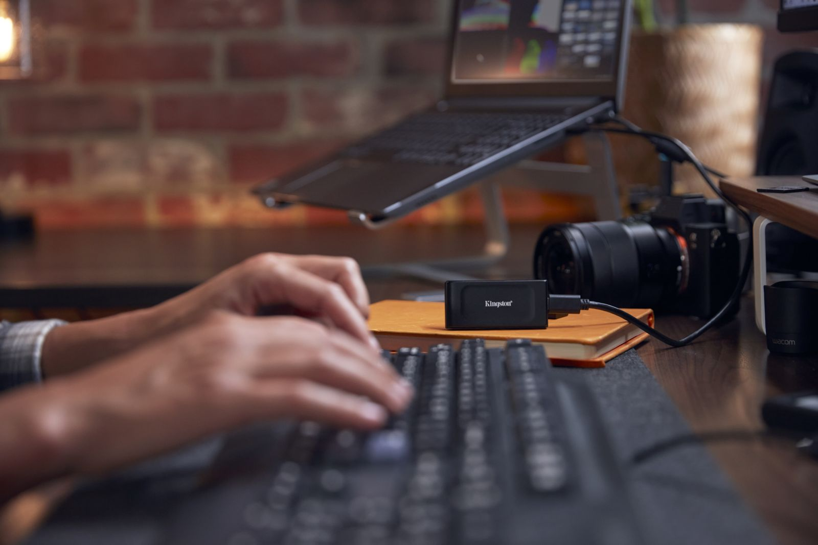 Ręce piszące na klawiaturze, obok laptopa i aparatu.