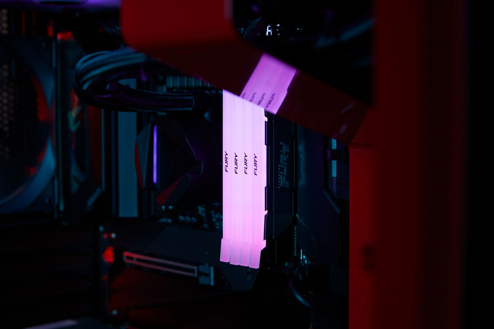 Pamięci RAM komputera z oświetleniem RGB w czerwonej obudowie, widoczne kable i komponenty.