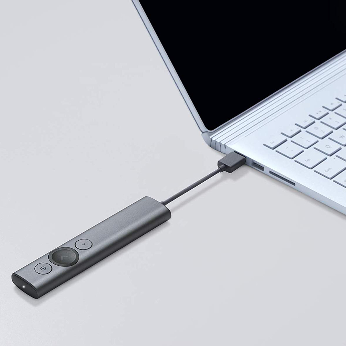A gray remote is connected to a white laptop with a USB cable on a white surface.