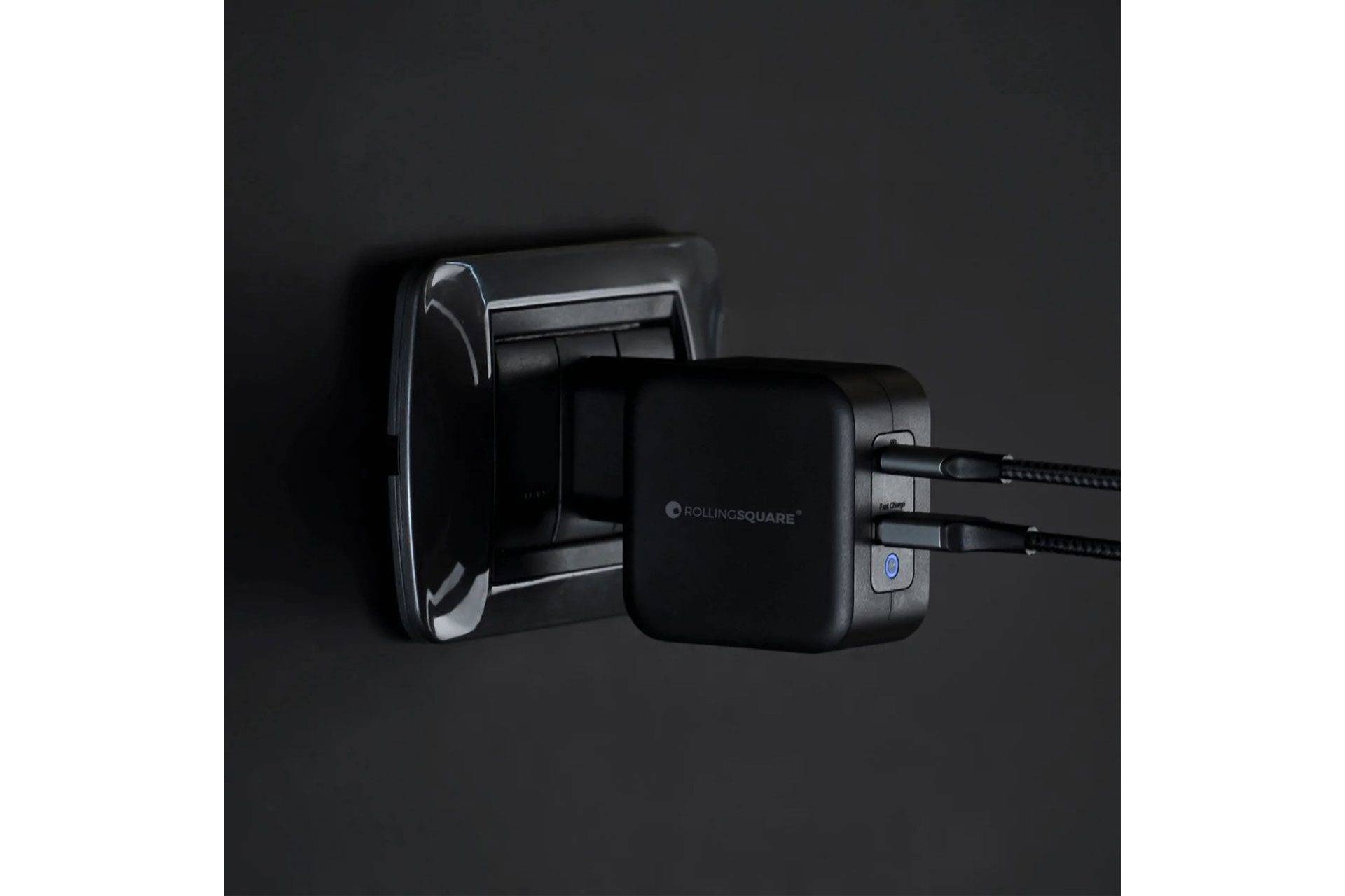 Zwarte oplader aangesloten op een stopcontact. De oplader heeft twee USB-poorten.