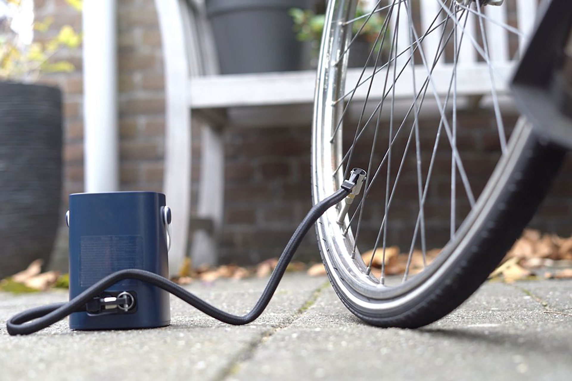 Een blauwe draagbare bandenpomp met een zwarte slang die een fietsband oppompt.