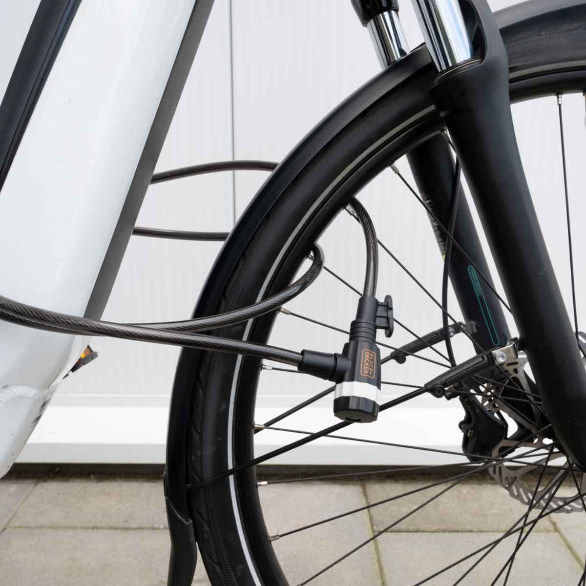 Een fietswiel met een zwart kabelslot eromheen. Het slot is aan het frame bevestigd.