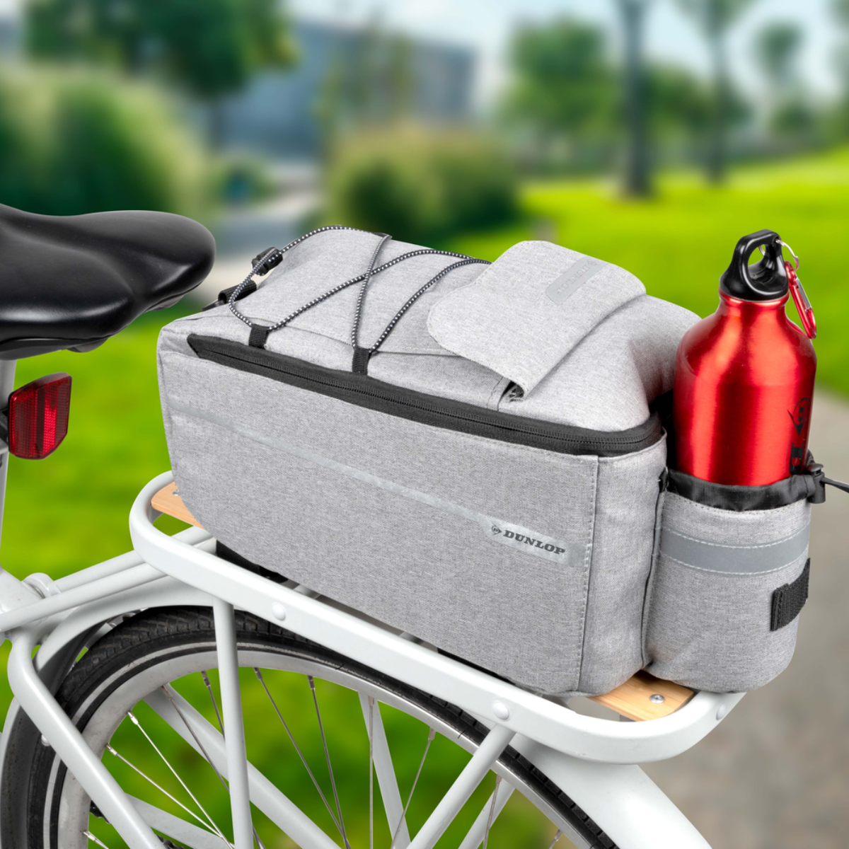 Een fiets met een grijze tas en een rode waterfles aan de achterste bagagedrager.