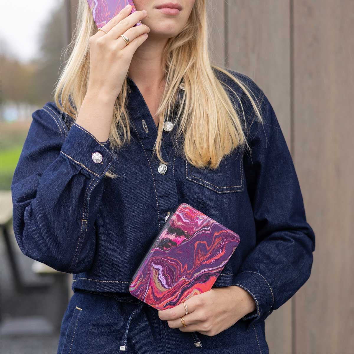 Femme en tenue en jean tenant un téléphone et un étui à motifs.